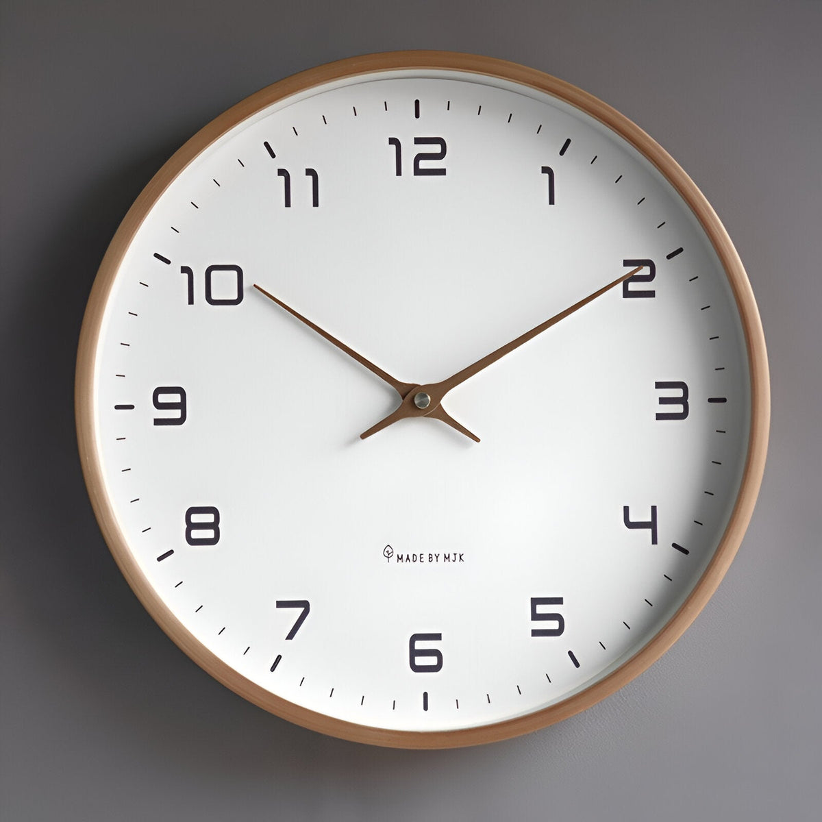 Nordic wall clock with light wood frame, white dial and brass hands on a grey wall