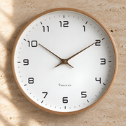 Nordic wall clock with light wood frame, white dial and brass hands on a warm travertine wall